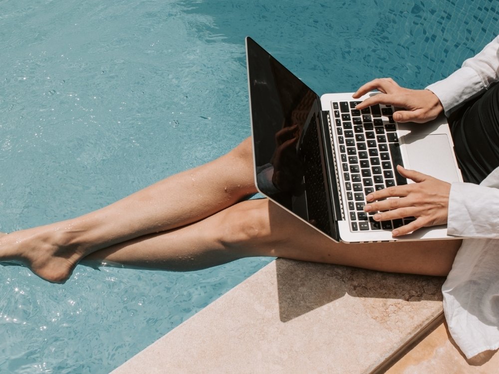 A woman works on her laptop by the pool. Plan a digital retreat around the seasons.