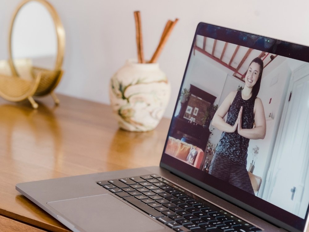 A woman practicing yoga while on a video call on her laptop during a wellness digital retreat.