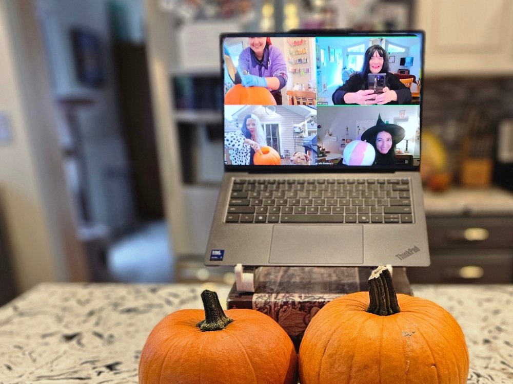 Two small pumpkins in front of a laptop open to a Zoom meeting where four people hold up pumpkins they have carved or painted.