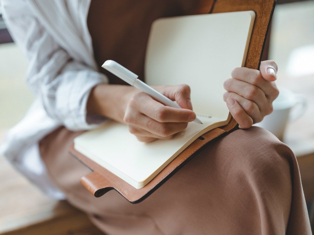 A woman journaling for creative inspiration. A tip from the blog, How to Avoid Burnout, Writer’s Block, and Creative Slumps by Hummingbird Marketing Services.