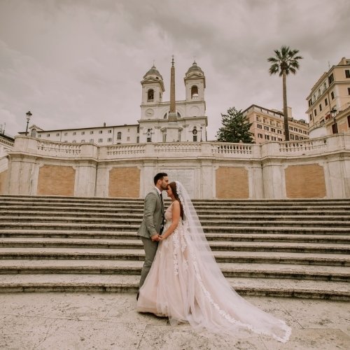 A bride and groom standing in front of a scenic view of stairs and buildings at their destination wedding.
