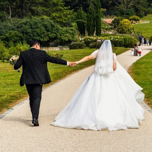 A husband and wife on their wedding day in a public park holding hands.